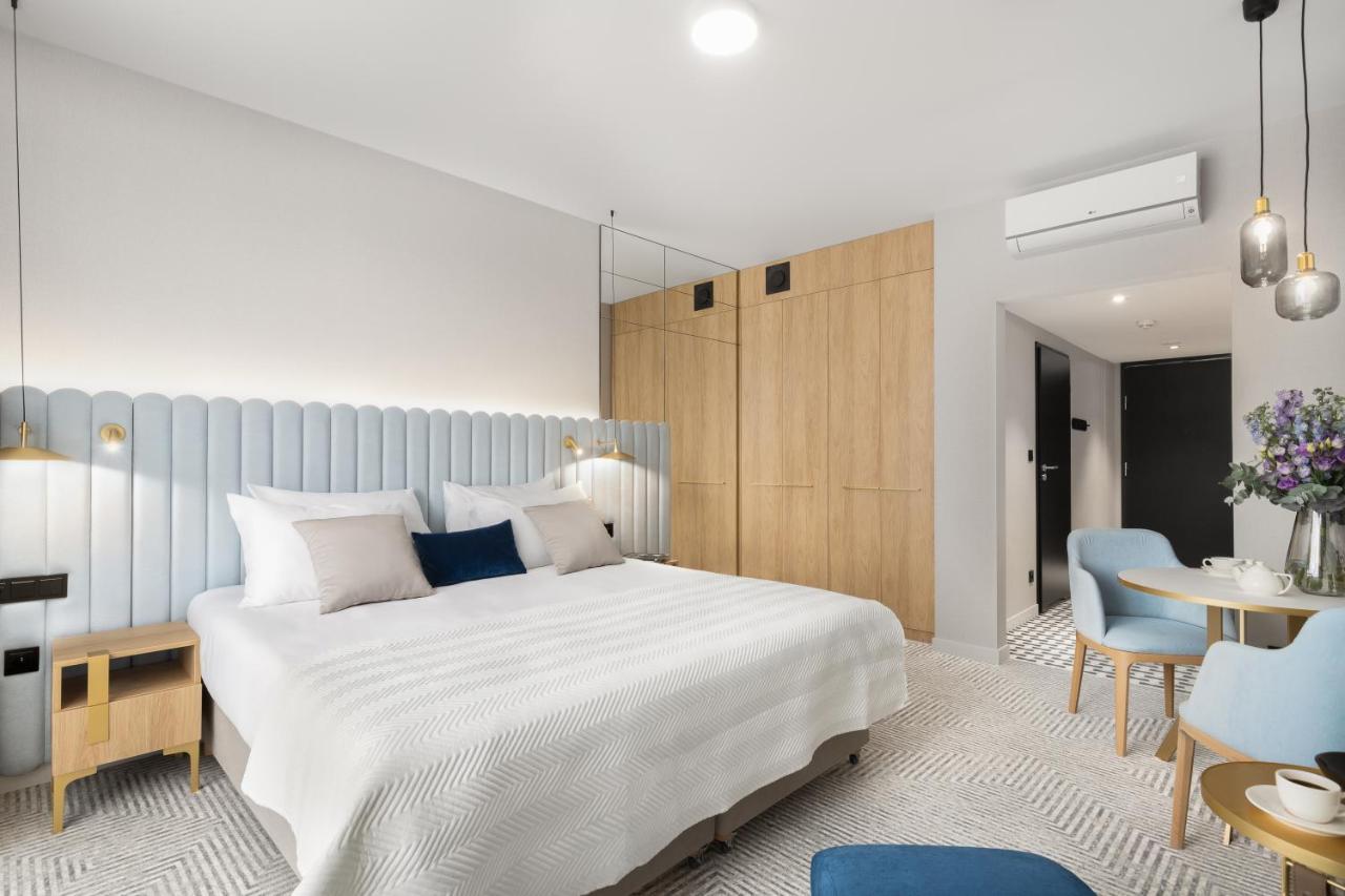 Royal Tulip Warsaw Centre Varsóvia Exterior foto The photo shows a modern hotel room featuring a spacious layout. There's a large double bed with a light-colored bedspread, accented by decorative pillows. The headboard is light blue, providing a soft contrast to the wooden walls. On one side of the