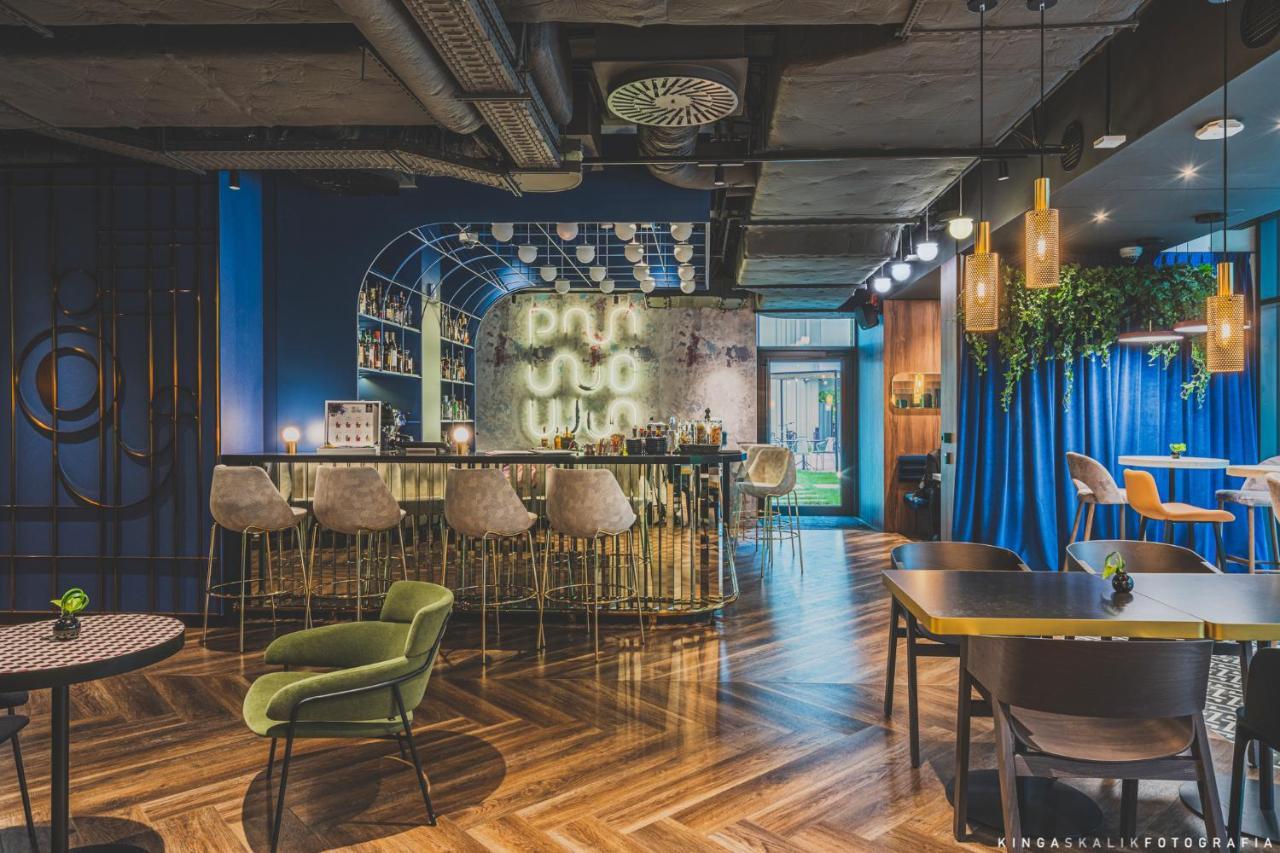 Royal Tulip Warsaw Centre Varsóvia Exterior foto The photo shows a modern and stylish bar or lounge area. It features a curved, elegant bar with high stools arranged in front. Behind the bar, there is a wall with mixed materials, partially illuminated, which likely showcases a selection of drinks. 