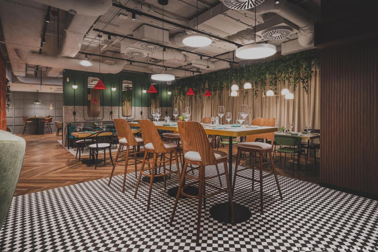 Royal Tulip Warsaw Centre Varsóvia Exterior foto The photo depicts a modern restaurant interior featuring a stylish design. There are high wooden bar stools arranged around a central table. The floor has a black and white checkered pattern, adding a classic touch. The walls are decorated with green