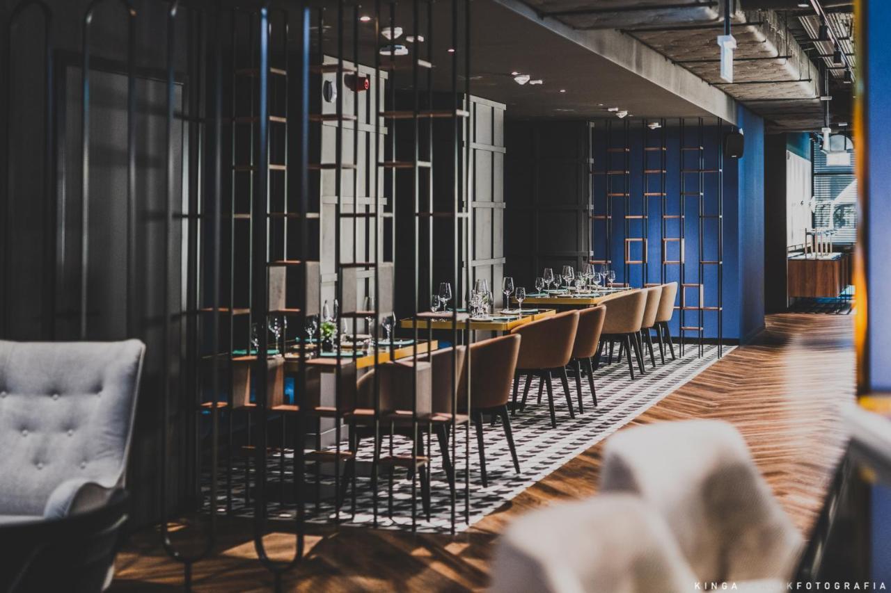 Royal Tulip Warsaw Centre Varsóvia Exterior foto The photo shows a modern restaurant interior. There are multiple dining tables arranged in a long line, each set with tableware and glassware. The space is divided by decorative metal partitions, creating an intimate atmosphere. The flooring features