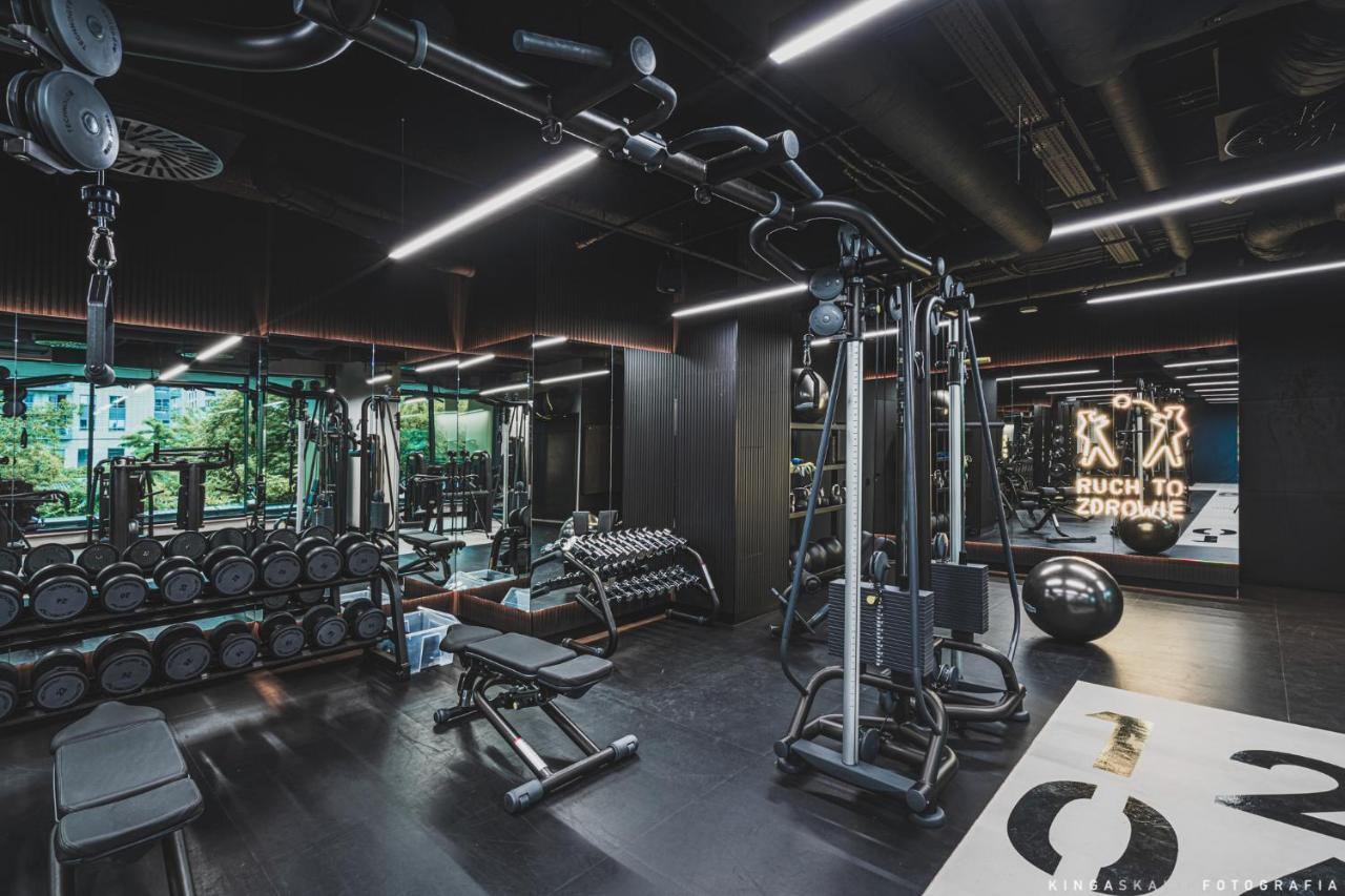 Royal Tulip Warsaw Centre Varsóvia Exterior foto The photo shows a modern gym interior. It features various fitness equipment including a multi-station machine for weight training, benches, and dumbbells. The space has a sleek design with dark colors and plenty of ambient lighting. In the backgroun