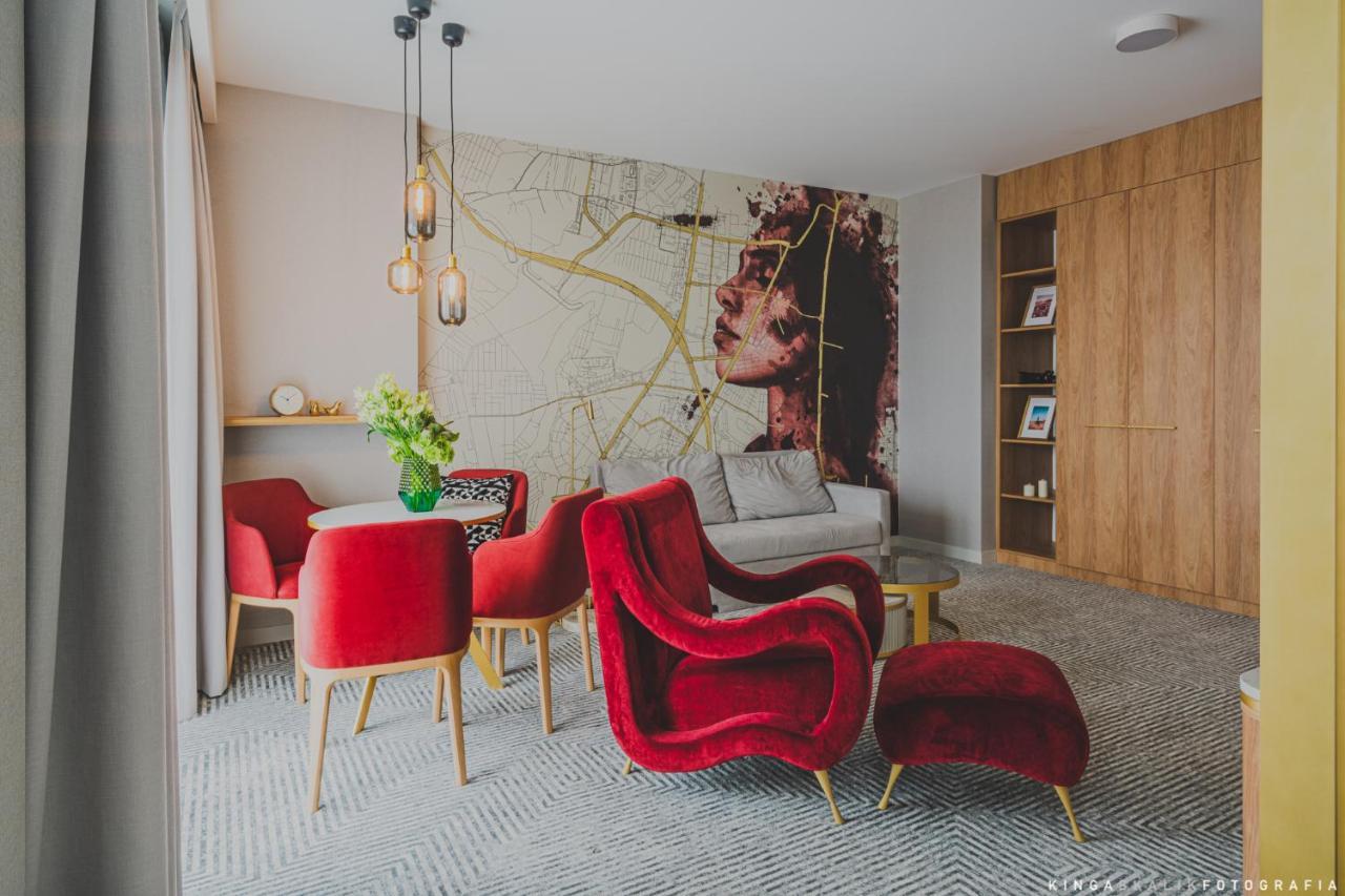Royal Tulip Warsaw Centre Varsóvia Exterior foto The photo shows a stylish and modern living space. The room features a large wall mural depicting a woman's face, which adds an artistic touch. In the foreground, there are several red armchairs with a plush design, complemented by a small round tabl