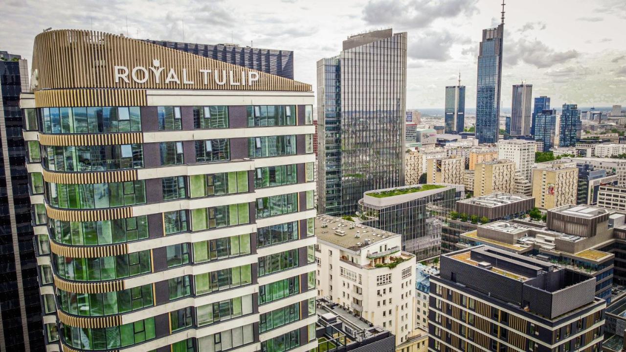 Royal Tulip Warsaw Centre Varsóvia Exterior foto The photo shows a cityscape featuring several modern skyscrapers and buildings. Prominently displayed in the foreground is the "Royal Tulip" hotel, characterized by its contemporary architectural design with large windows. Surrounding it are other ta