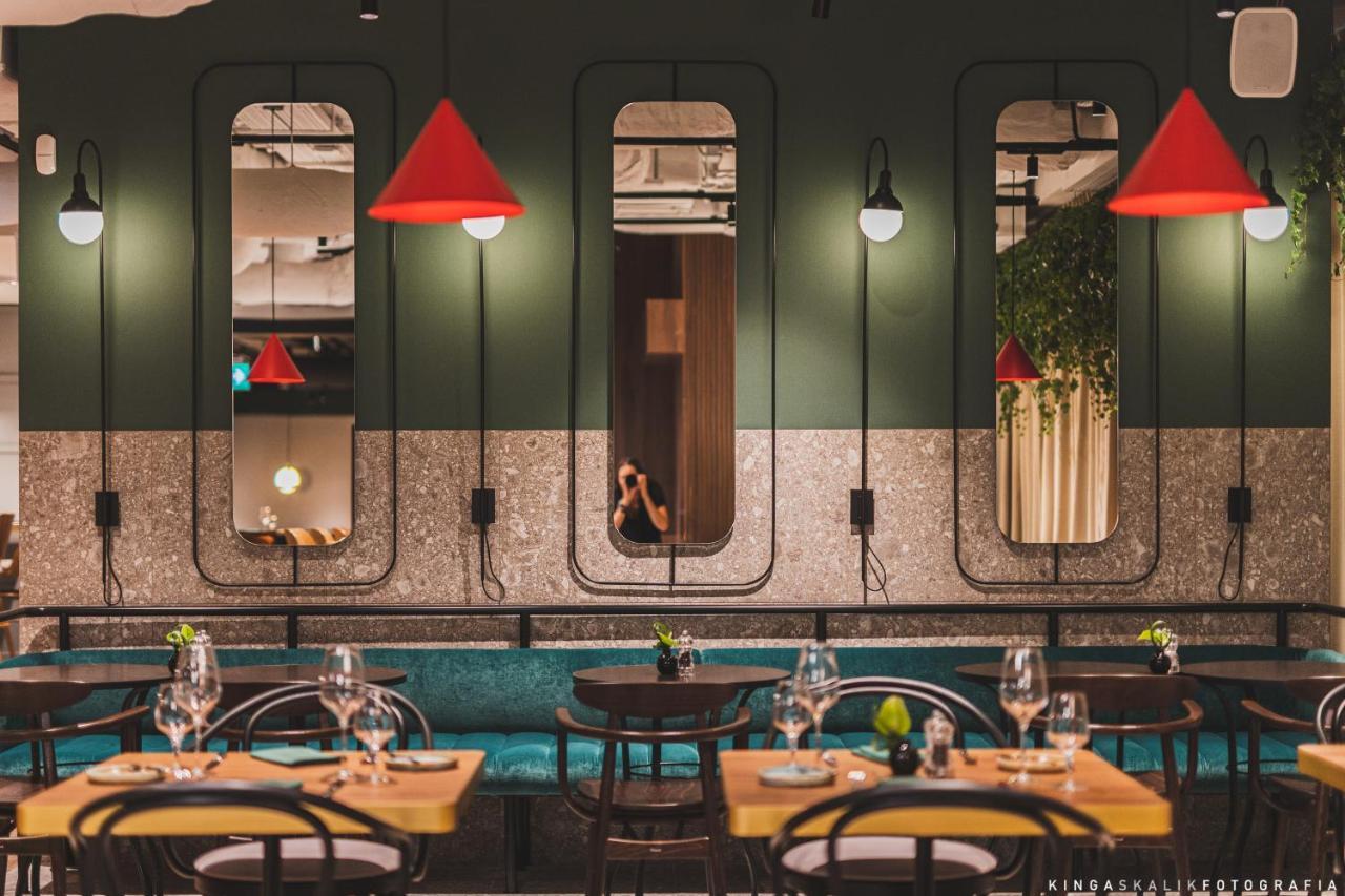 Royal Tulip Warsaw Centre Varsóvia Exterior foto The photo depicts a modern restaurant interior characterized by a stylish design. The walls are painted in dark green, featuring several mirrors set in unique frames. Bright red pendant lights hang from the ceiling, adding a pop of color to the space