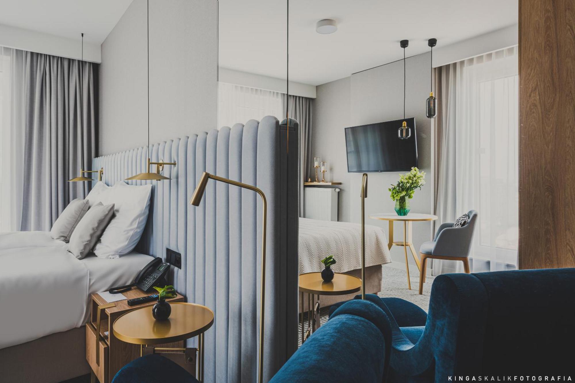 Royal Tulip Warsaw Centre Varsóvia Exterior foto The photo shows a modern hotel room featuring a stylish and contemporary design. In the foreground, there is a bed with a plush, upholstered headboard and white bedding. Beside the bed, there are sleek wooden bedside tables with small plants on top.
