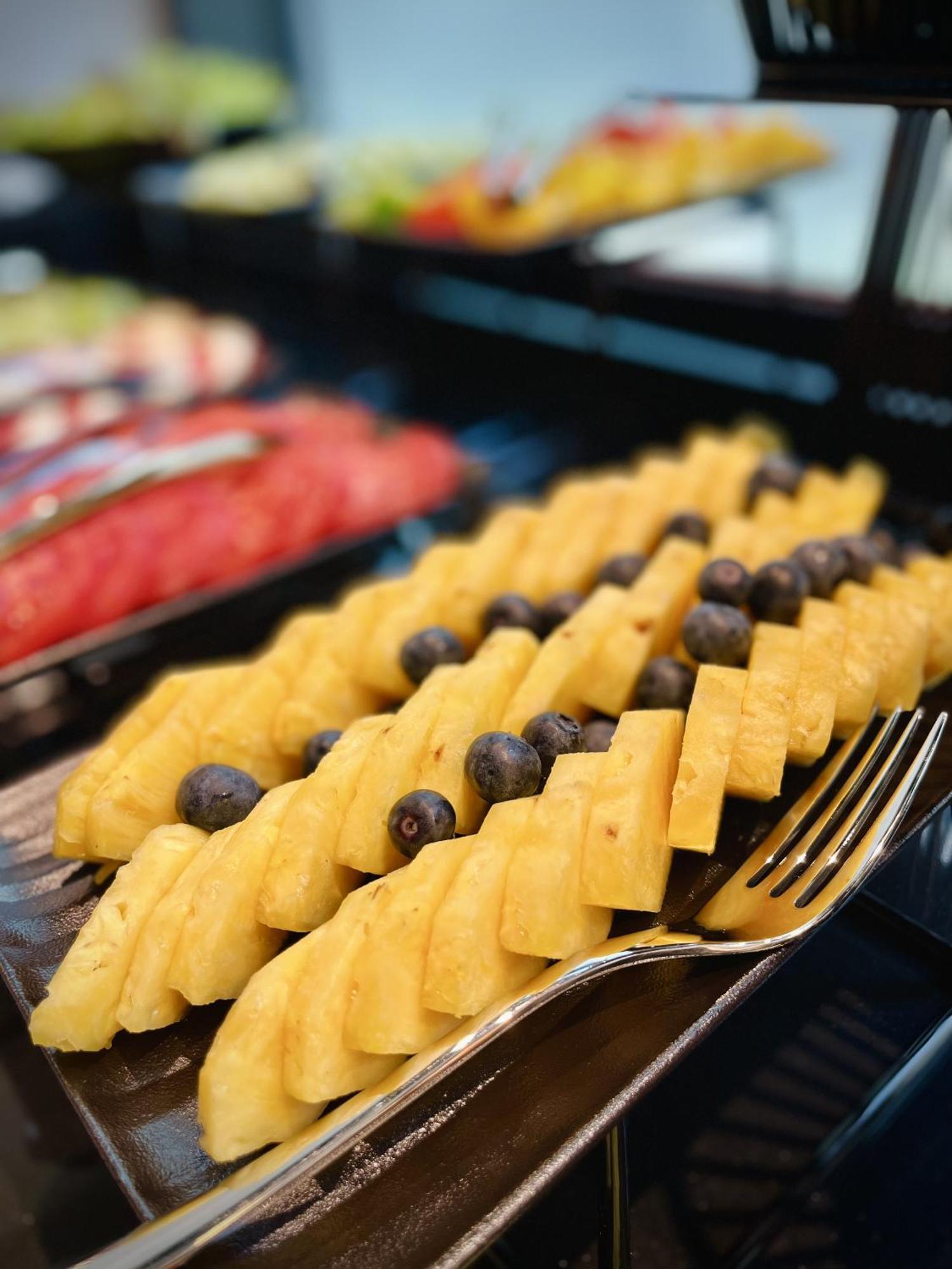 Royal Tulip Warsaw Centre Varsóvia Exterior foto The photo shows a colorful fruit display featuring neatly arranged slices of yellow pineapple, interspersed with dark blueberries. The pineapple slices are cut into a checkerboard pattern, creating an appealing presentation. In the background, other 