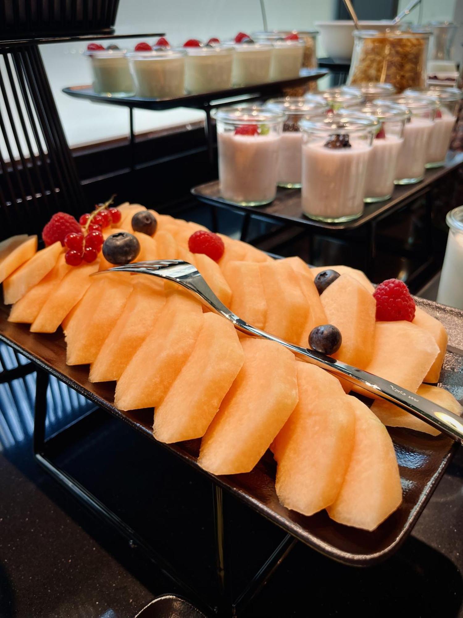 Royal Tulip Warsaw Centre Varsóvia Exterior foto The photo features a platter of sliced cantaloupe, arranged neatly and garnished with a few berries. There are red raspberries and blueberries placed on top of the melon slices. In the background, there are cups of dessert, likely some type of puddin