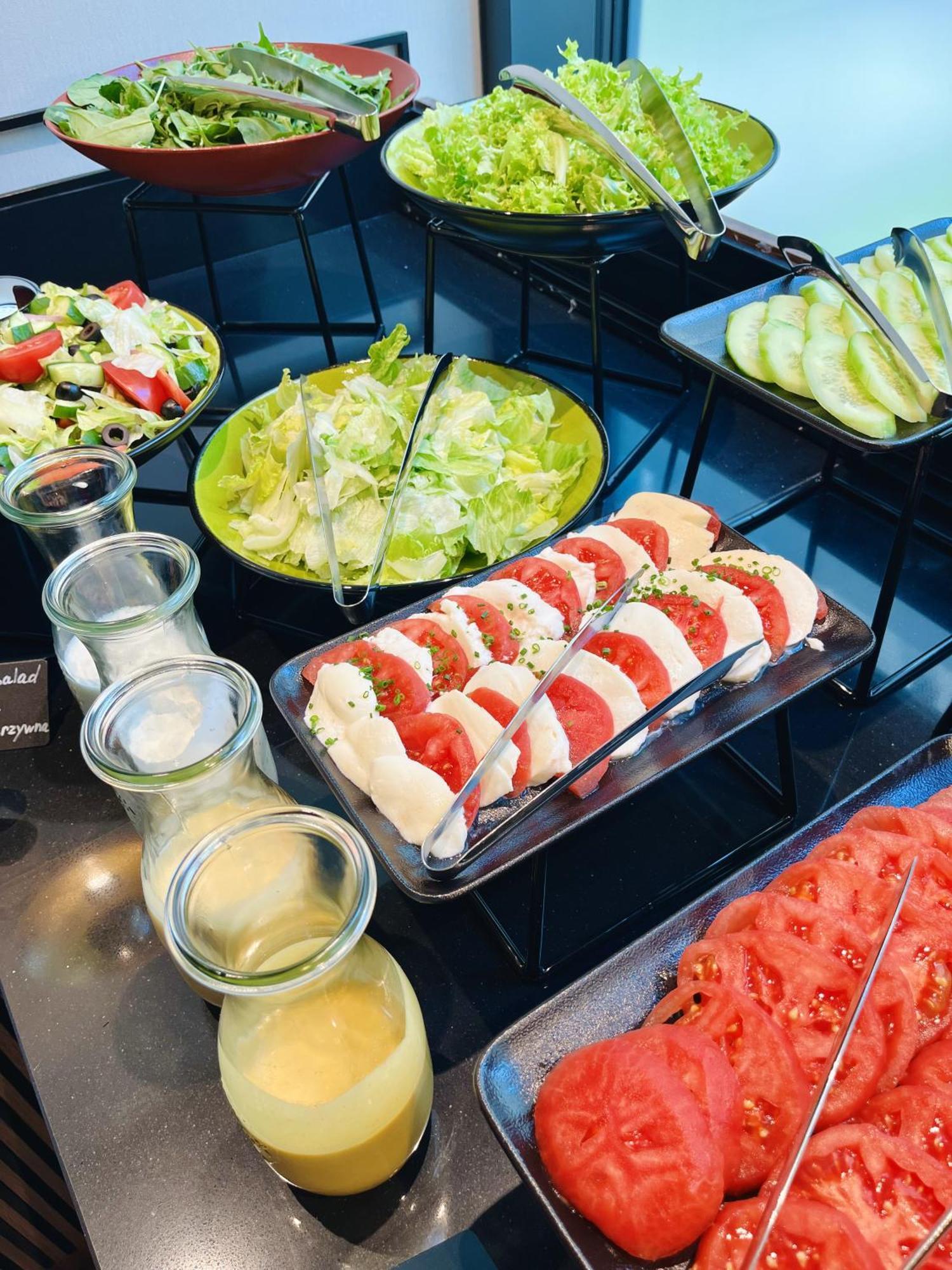 Royal Tulip Warsaw Centre Varsóvia Exterior foto The photo displays a buffet-style arrangement of various salads and ingredients. Specifically, there is a fresh green salad with lettuce and possibly additional vegetables in a large green bowl. In front, there is a platter featuring slices of mozzar