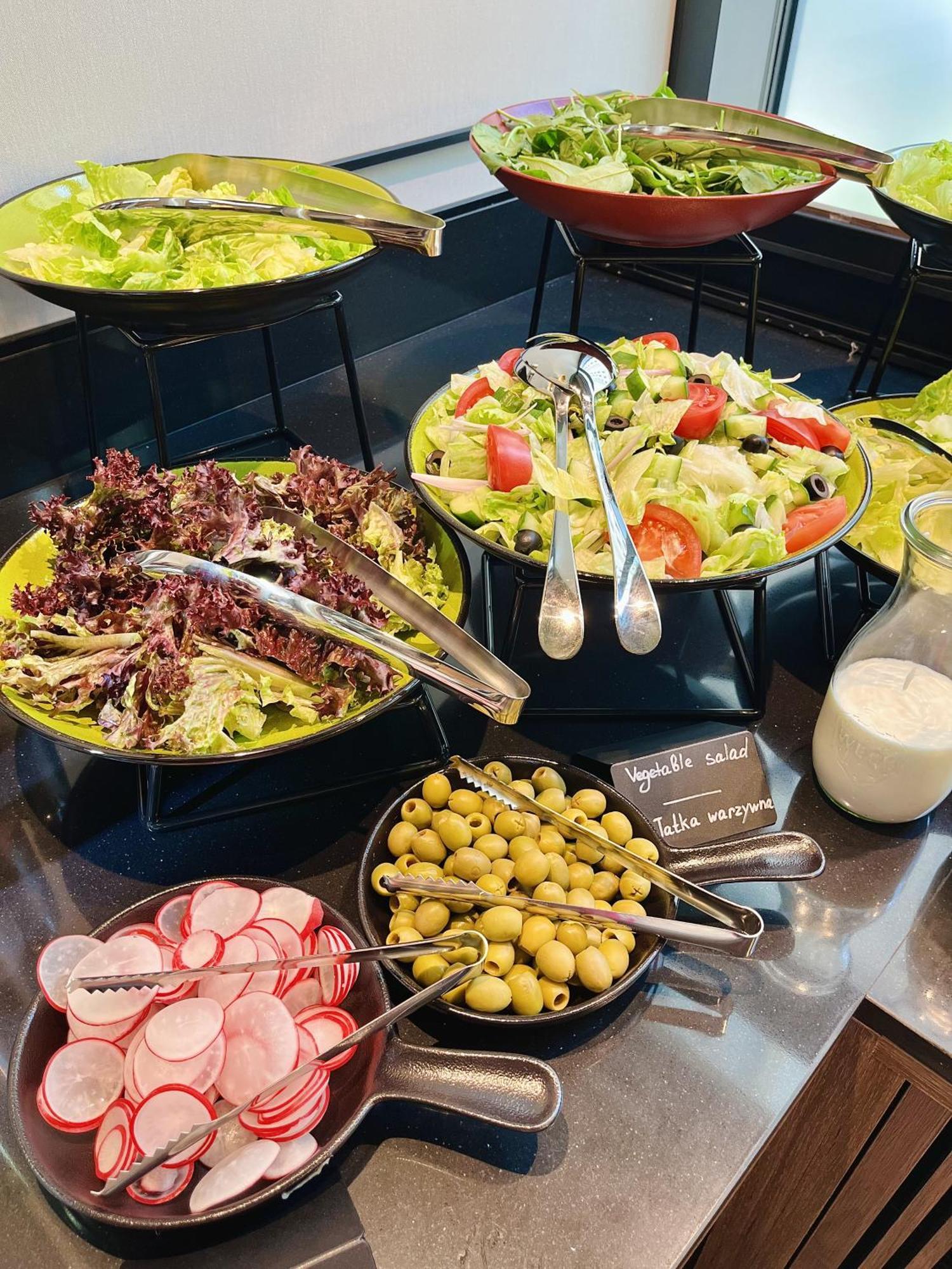 Royal Tulip Warsaw Centre Varsóvia Exterior foto The photo shows a variety of salad options arranged on a table. 

1. **Salads**: There are two larger bowls—one with mixed greens, including red leaf lettuce, and another with a colorful salad that includes chopped tomatoes, cucumbers, and olives.
2.