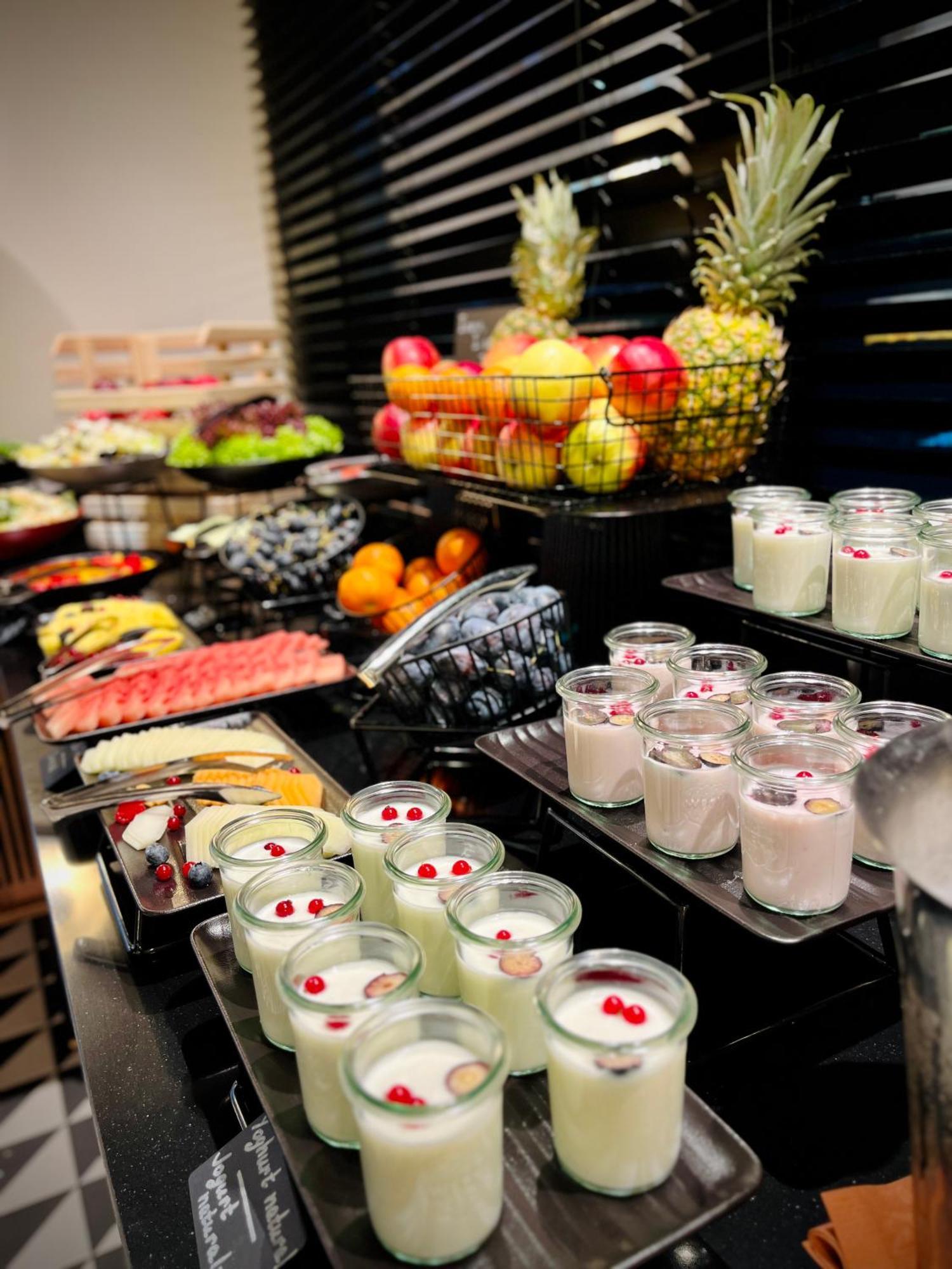 Royal Tulip Warsaw Centre Varsóvia Exterior foto The photo displays an assortment of food items arranged on a buffet table. In the foreground, there are several small glass containers filled with creamy desserts, garnished with red berries. Behind them, various fruits are presented, including apple