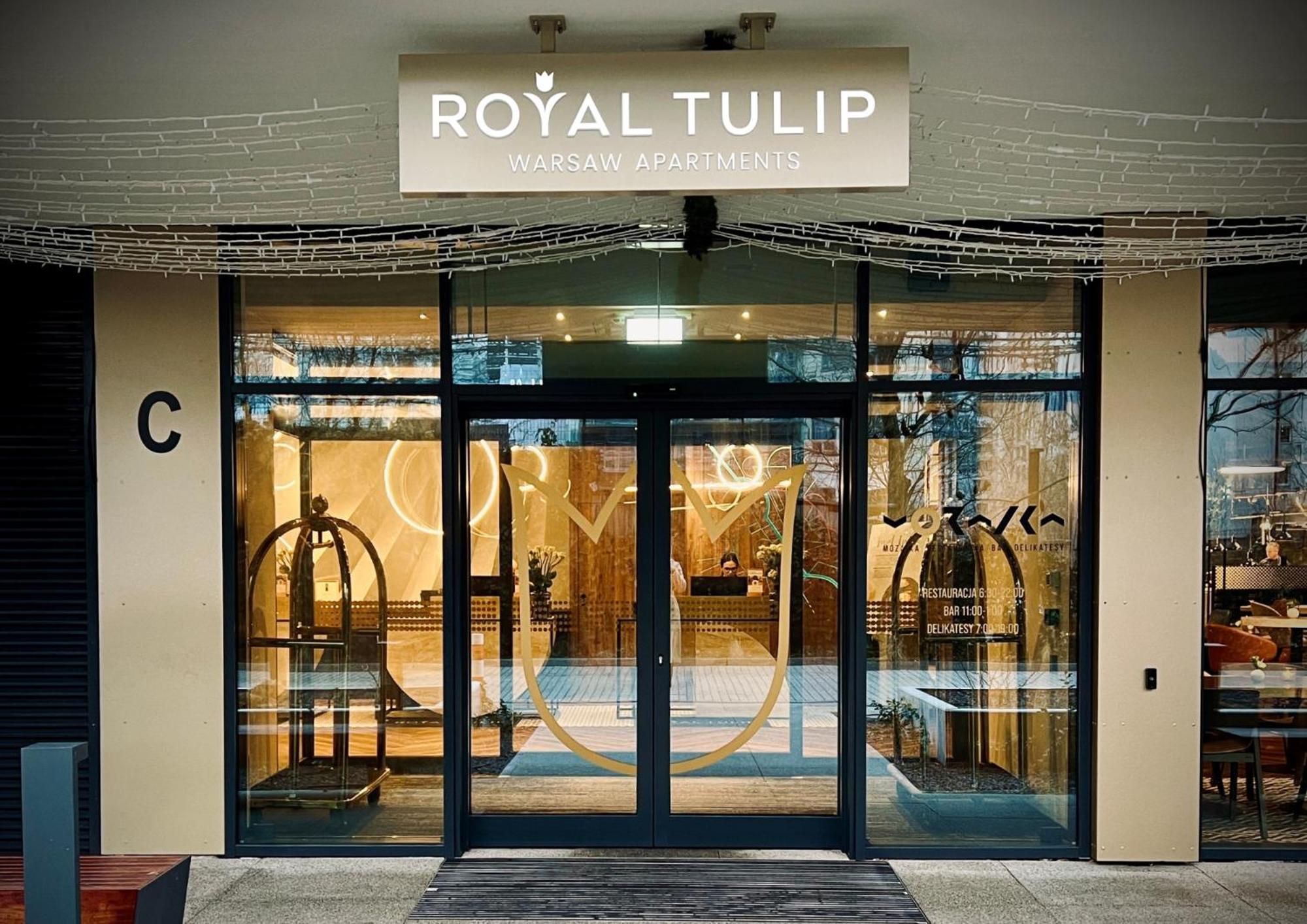 Royal Tulip Warsaw Centre Varsóvia Exterior foto The photo shows the entrance to a hotel named "Royal Tulip." The facade features large glass doors that allow a view into the lobby area. There are decorative elements, including what appears to be luggage carts near the entrance. Above the doors is 