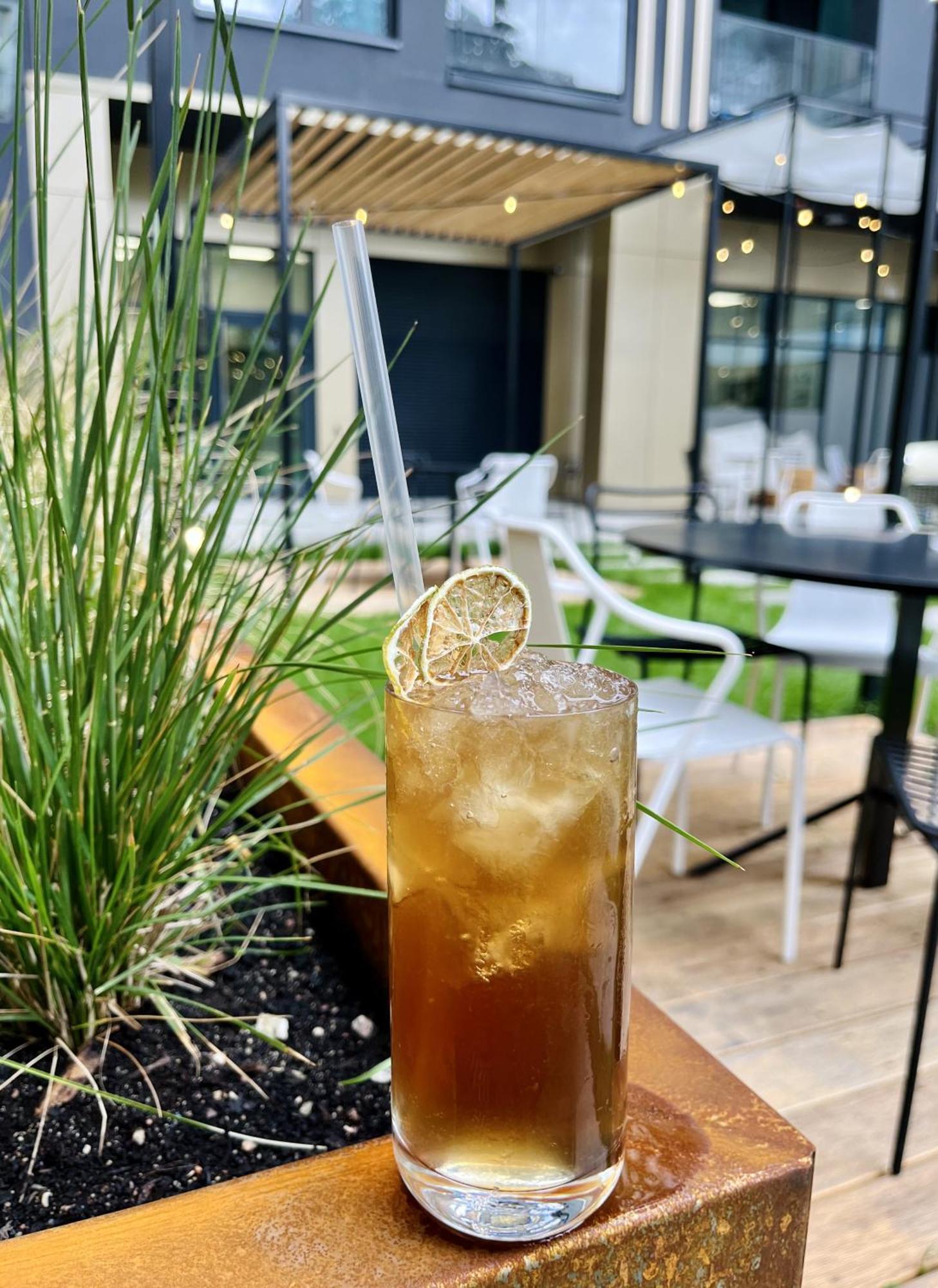Royal Tulip Warsaw Centre Varsóvia Exterior foto The photo shows a tall glass filled with a dark, fizzy drink, likely a cocktail or a refreshing beverage. It is filled with ice cubes and has a straw for drinking. A slice of dried lime is placed on the rim of the glass, adding a decorative touch. In