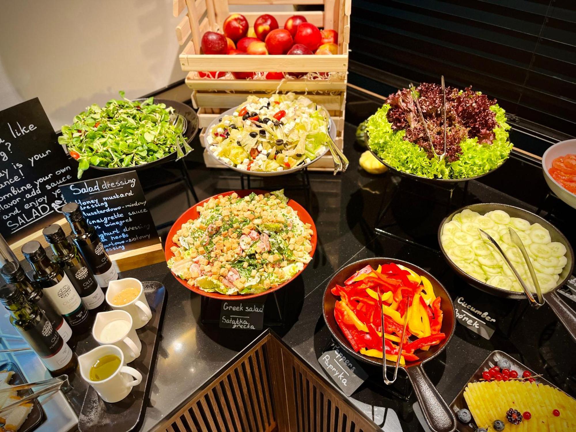 Royal Tulip Warsaw Centre Varsóvia Exterior foto The photo shows a well-arranged salad bar featuring a variety of fresh salads and ingredients. There are several bowls and dishes with different types of salads, including green salads and grain salads. 

1. **Green Salads**: There are multiple bowls