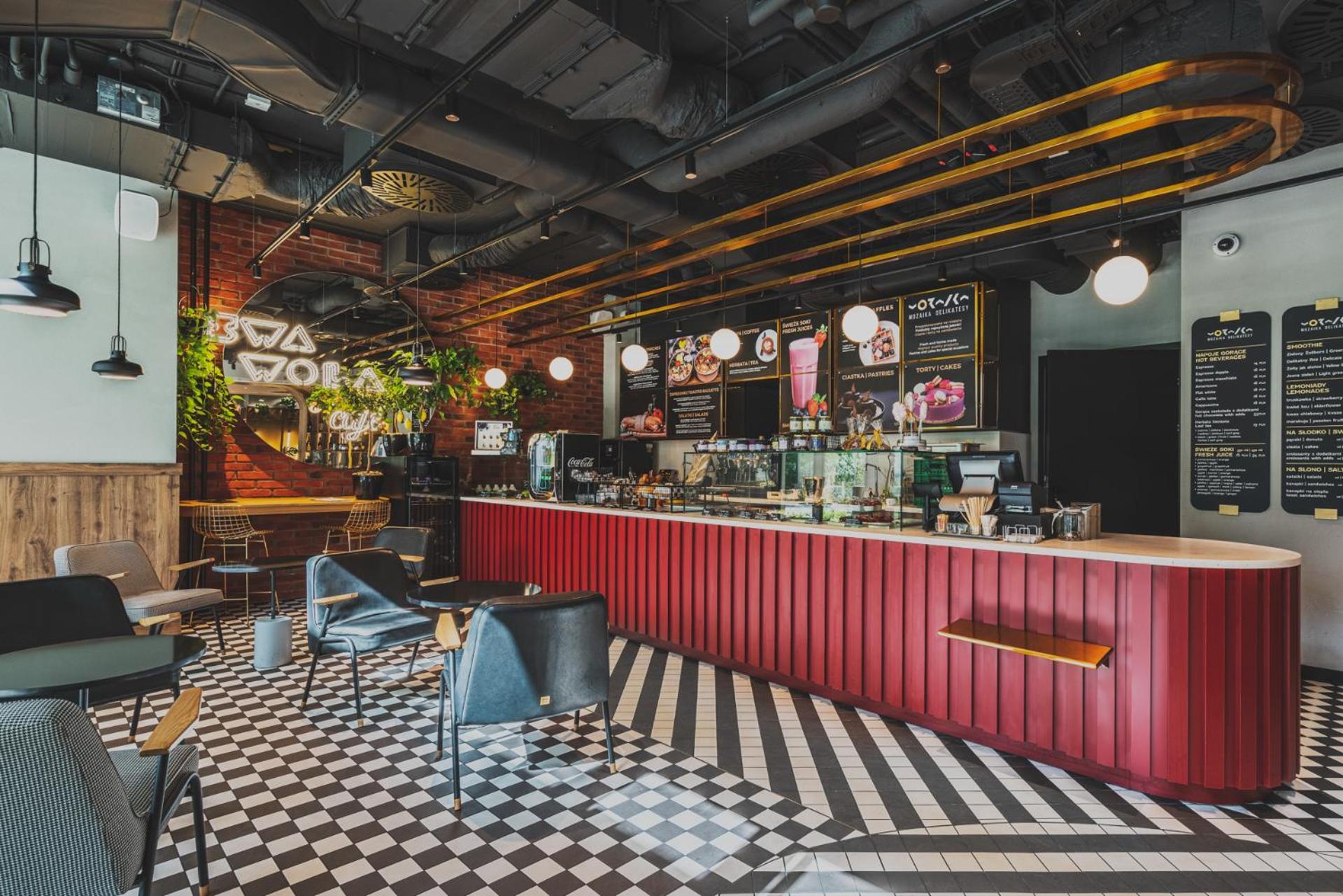 Royal Tulip Warsaw Centre Varsóvia Exterior foto The photo shows a modern café interior. There is a prominent red counter that stretches across the space, where a variety of beverages and snacks are displayed. Behind the counter, there are menus and a selection of products. The flooring features a 
